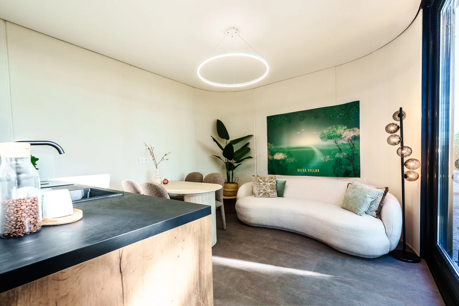 Compacte woonkamer met ronde bank, eettafel en licht door de glazen gevel